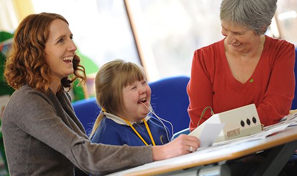 A young girl with Downs Syndrome using the speech and language therapy equipment with two adults
