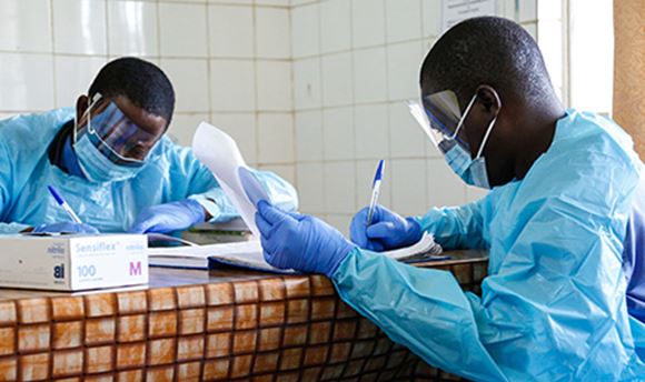Two nurses in full PPE sitting at a table together filling in paperwork 