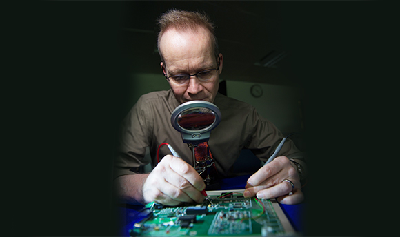 A man working on electronics through a magnifying glass
