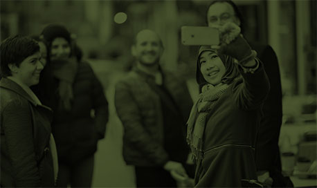 A group of six international students pose for a selfie together in Edinburgh city centre. A dark green tint covers the photograph.